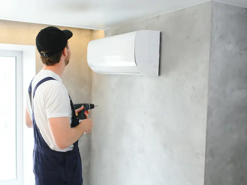 Technicien fixant une unité murale de climatisation au mur d'une pièce