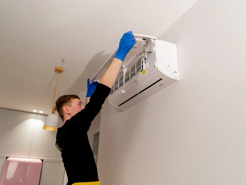 Technicien nettoyant en hauteur un split mural et son évacuation