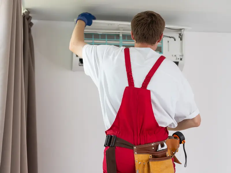 Technicien réalisant l'entretien d'une climatisation murale dans une chambre